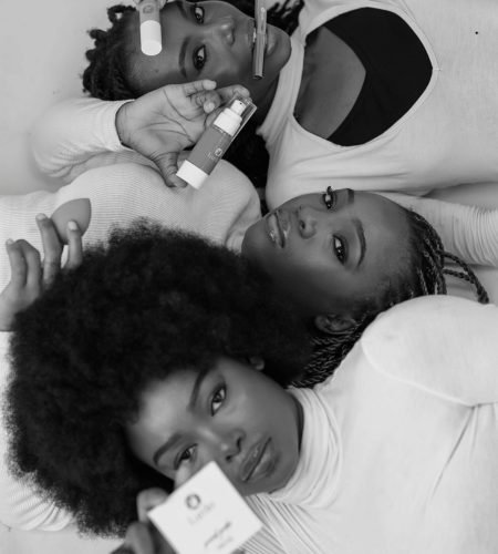 Black and white portrait of three women holding skincare and beauty products in a graceful pose.