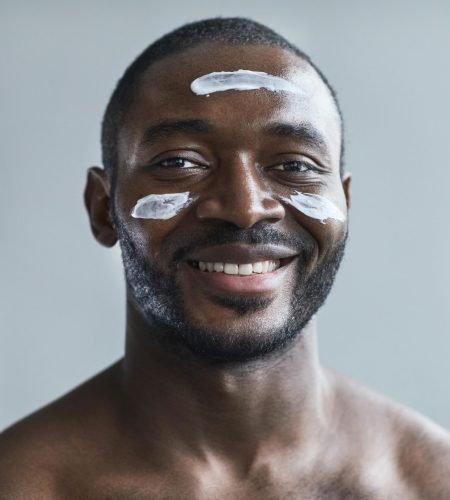 Close-up of a smiling black man applying face cream with a happy expression.